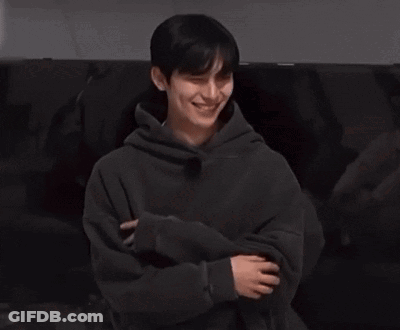 Young Man In Black Hoodie Sitting On Couch Holding Cell Phone GIF