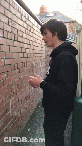 Young Man In Black Hoodie With Letter N At Brick Wall GIF