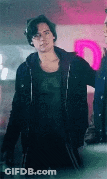 Young Man In Black Jacket And Beanie In Front Of Neon Sign GIF