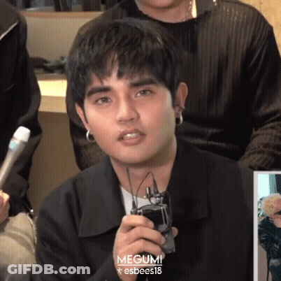 Young Man In Black Jacket And Earrings Holding Microphone And Cell Phone GIF
