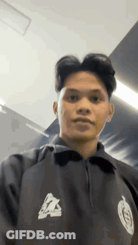 Young Man In Black Jacket Standing By Wall GIF