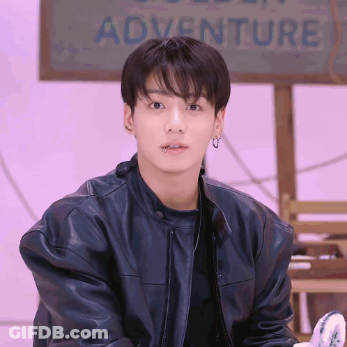 Young Man In Black Leather Jacket And Earrings In Front Of Adventure Sign GIF