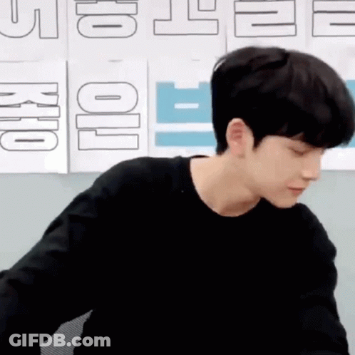 Young Man In Black Shirt Sitting By Wall With Signs GIF
