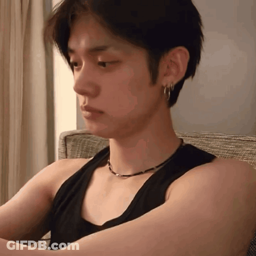 Young Man In Black Tank Top And Earrings Sitting On Couch GIF