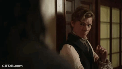 Young Man In Black Vest And Tie By Door In Dark Room GIF