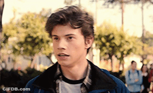 Young Man In Blue Jacket And Plaid Shirt Standing By Trees GIF