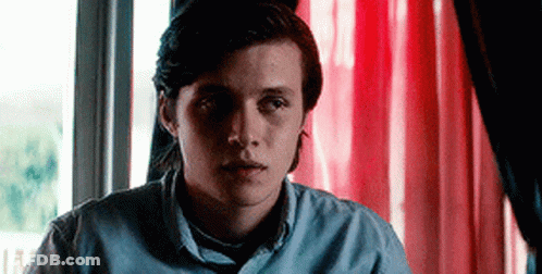Young Man In Blue Shirt Sitting By Window With Red Curtain GIF