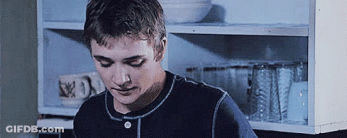 Young Man In Blue Shirt Standing In Front Of Shelf GIF