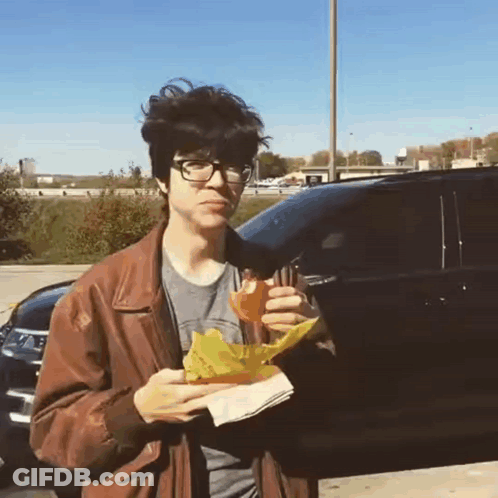 Young Man In Brown Jacket Eating Sandwich GIF