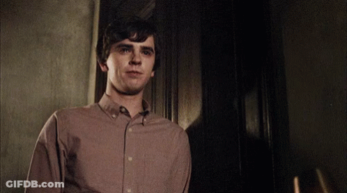Young Man In Brown Shirt Standing In Dark Room GIF