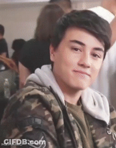 Young Man In Camouflage Jacket Sitting In Crowd GIF