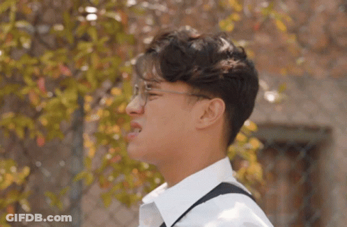 Young Man In Glasses And White Shirt Standing By Fence GIF