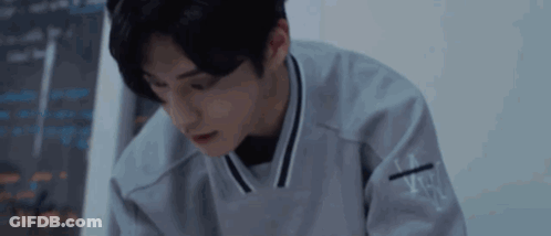 Young Man In Gray Sweater Sitting At Table In Dark Room GIF