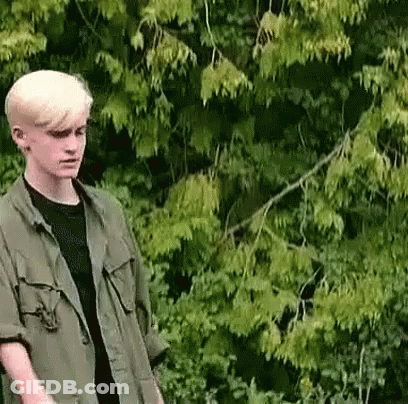 Young Man In Green Jacket And Black Shirt Standing Before Tree GIF
