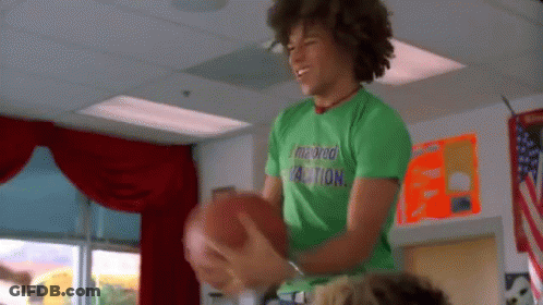 Young Man In Green Shirt Holding Football In Classroom GIF
