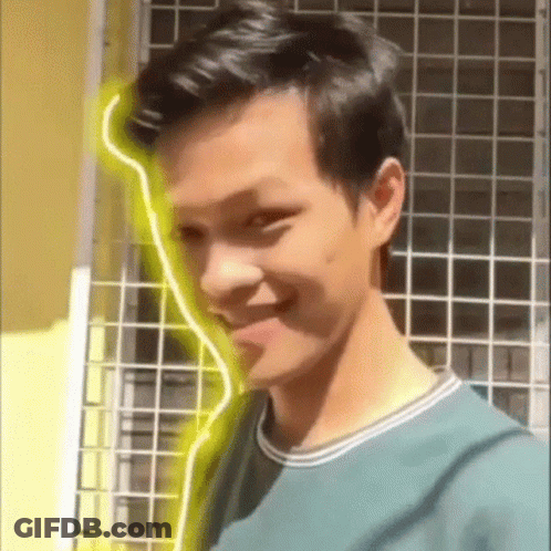 Young Man In Green Shirt Smiling In Front Of Yellow Light GIF