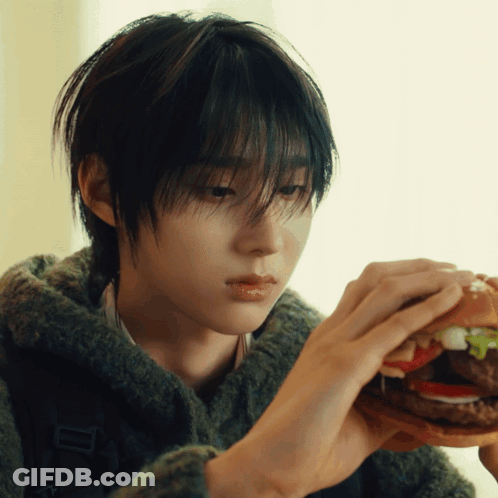 Young Man In Green Sweater Eating Hamburger With Lettuce And Tomato GIF