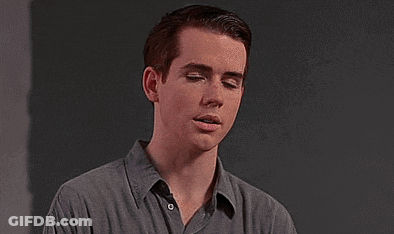 Young Man In Grey Shirt Against Black Wall GIF