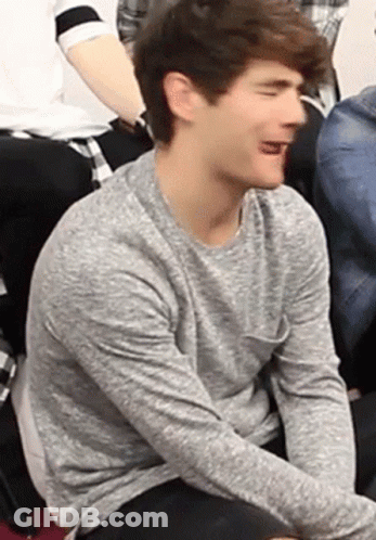 Young Man In Grey Sweater Sitting With Tongue Out GIF