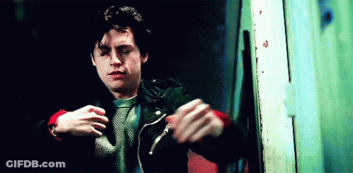 Young Man In Leather Jacket And Red Sweater Standing In Front Of Door GIF