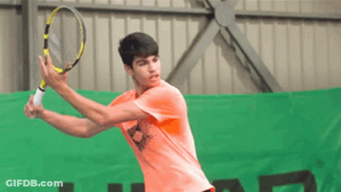 Young Man In Orange Shirt Swinging Tennis Racquet GIF