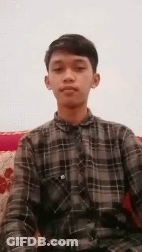 Young Man In Plaid Shirt Sitting On Couch Looking At Camera GIF