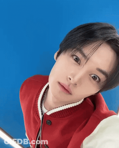 Young Man In Red Jacket Looking Up Against Blue Background GIF