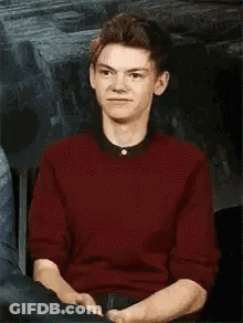 Young Man In Red Sweater Sitting With Hands Folded GIF