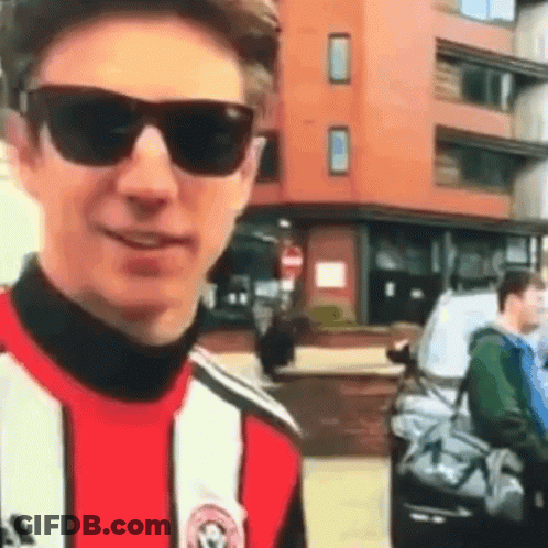 Young Man In Sunglasses And Striped Shirt Standing In Front Of Building GIF