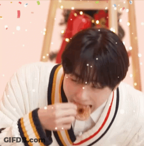 Young Man In Sweater Eating Donut With Confetti GIF