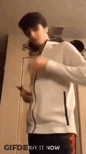 Young Man In White Jacket Holding Cell Phone By Door GIF