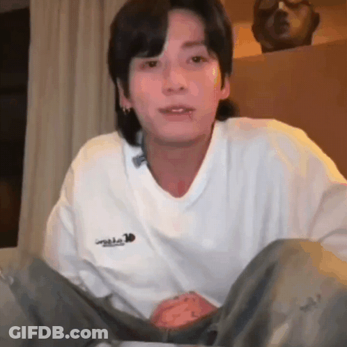 Young Man In White Sweater Sitting On Bed GIF