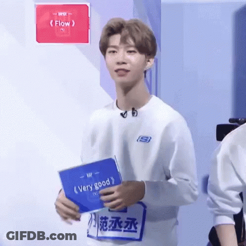 Young Man In White Sweatshirt Holding Blue Book GIF