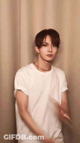 Young Man In White T-Shirt And Necklace Standing Before Curtain GIF