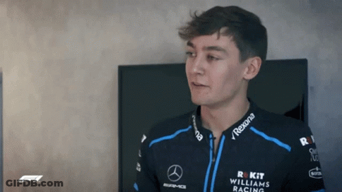 Young Man In Williams Racing Jacket Standing Before TV GIF