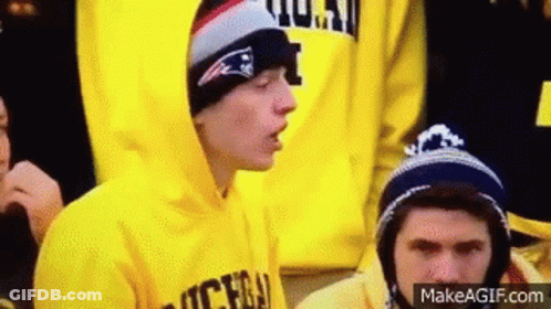 Young Man In Yellow Hoodie And Hat Sitting In Crowd GIF