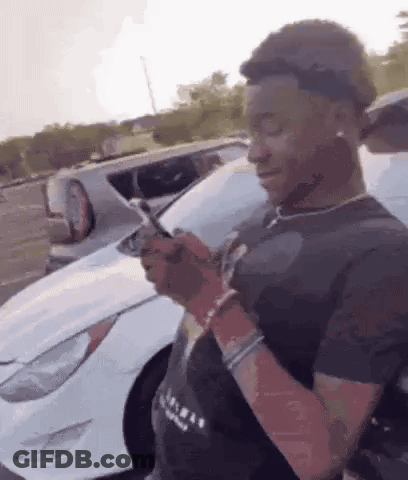 Young Man Looking At Phone In Front Of White Car GIF