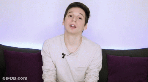 Young Man On Couch With Purple Pillows Gesturing GIF