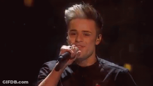 Young Man Singing Into Microphone On Stage GIF
