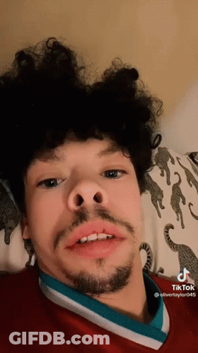 Young Man With Curly Hair And Beard Laying On Bed GIF