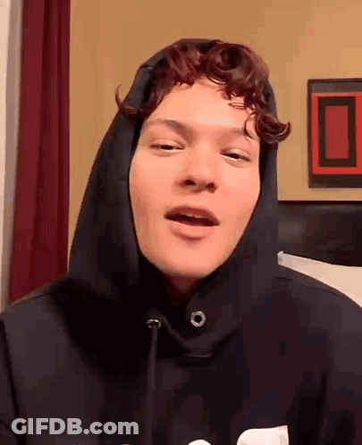Young Man With Curly Hair In Black Hoodie Talking To Camera GIF