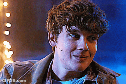 Young Man With Curly Hair Smiling In Front Of Blue Background With Lights GIF