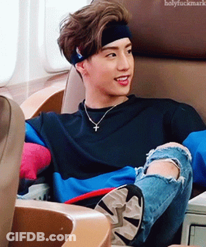 Young Man With Headband And Necklace Sitting In Chair GIF