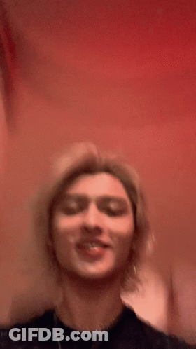 Young Man With Long Blonde Hair Smiling In Black Shirt GIF