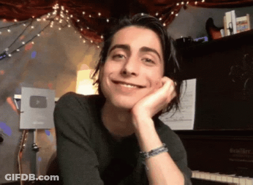 Young Man With Long Hair Smiling At Piano GIF