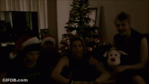 Young Men Wearing Santa Hats By Christmas Tree GIF