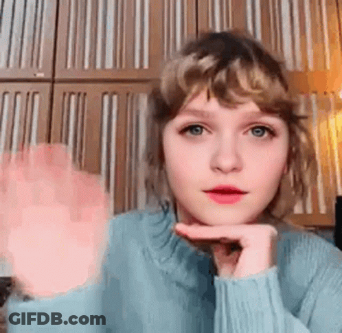Young Woman In Blue Sweater Waving Hand Near Striped Wall GIF