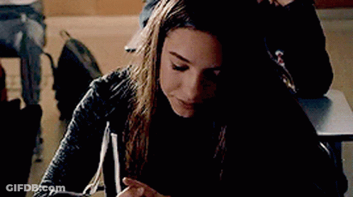 Young Woman Sitting At Desk Looking At Phone GIF