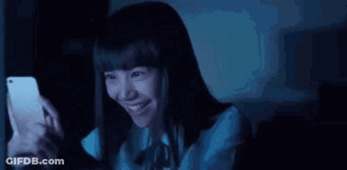 Young Woman Smiling At Phone In Dark GIF