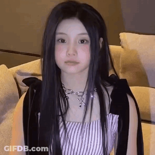 Young Woman With Long Black Hair Sitting On Couch In Striped Top And Necklace GIF